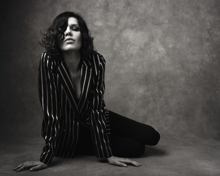 Black and white fashion portrait of women sitting on the floor wearing a pin stripe jacket.